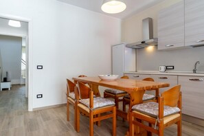 A modern kitchen with a dining area, wooden table, chairs, and a white refrigerator.
