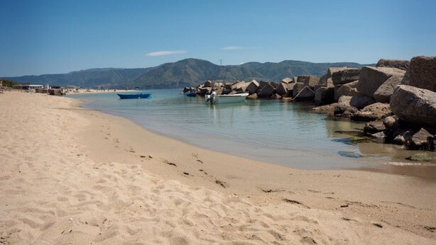 A beach with a rocky shoreline, clear blue water, and mountains in the background.