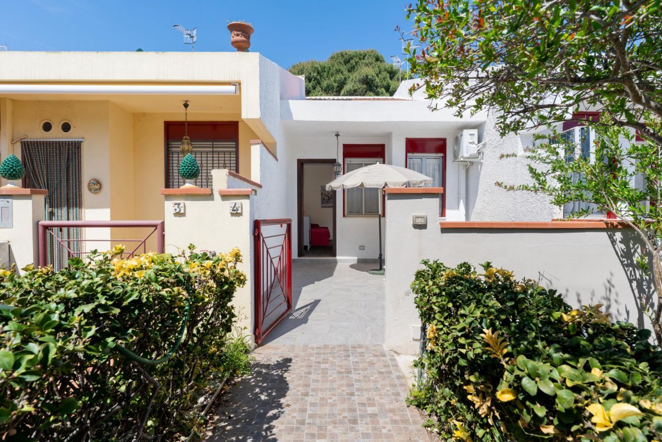 A white building with a tiled entrance, a red gate, and a small red door.
