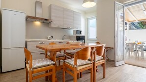 A modern kitchen with a dining area, wooden chairs, a white refrigerator, and a microwave.