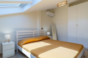 A bedroom with a bed, nightstand, bedside lamp, wardrobe, and skylight.