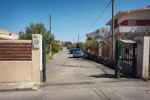 A residential street with houses on both sides, a gate with a sign, and parked cars.