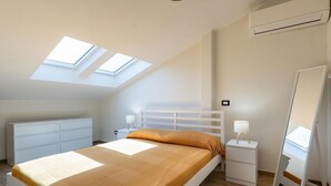 A bedroom with a bed, two bedside tables, a nightstand, a mirror, and skylights.