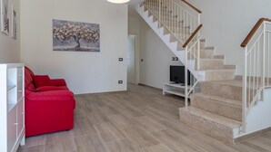 A living room with a red sofa, a painting, a TV, and a staircase.