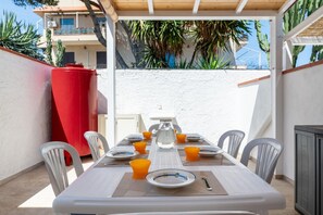 An outdoor dining area with a table set for four, surrounded by white chairs, a red planter, and a white wall. - A comfortable 90 sqm apartment on two levels connected by an internal staircase, ideal for up to 6 people.The property is located in Torre Faro, one of the most picturesque towns in the Messina area, about 15 km from the center of Messina, at a point whe (Messina)