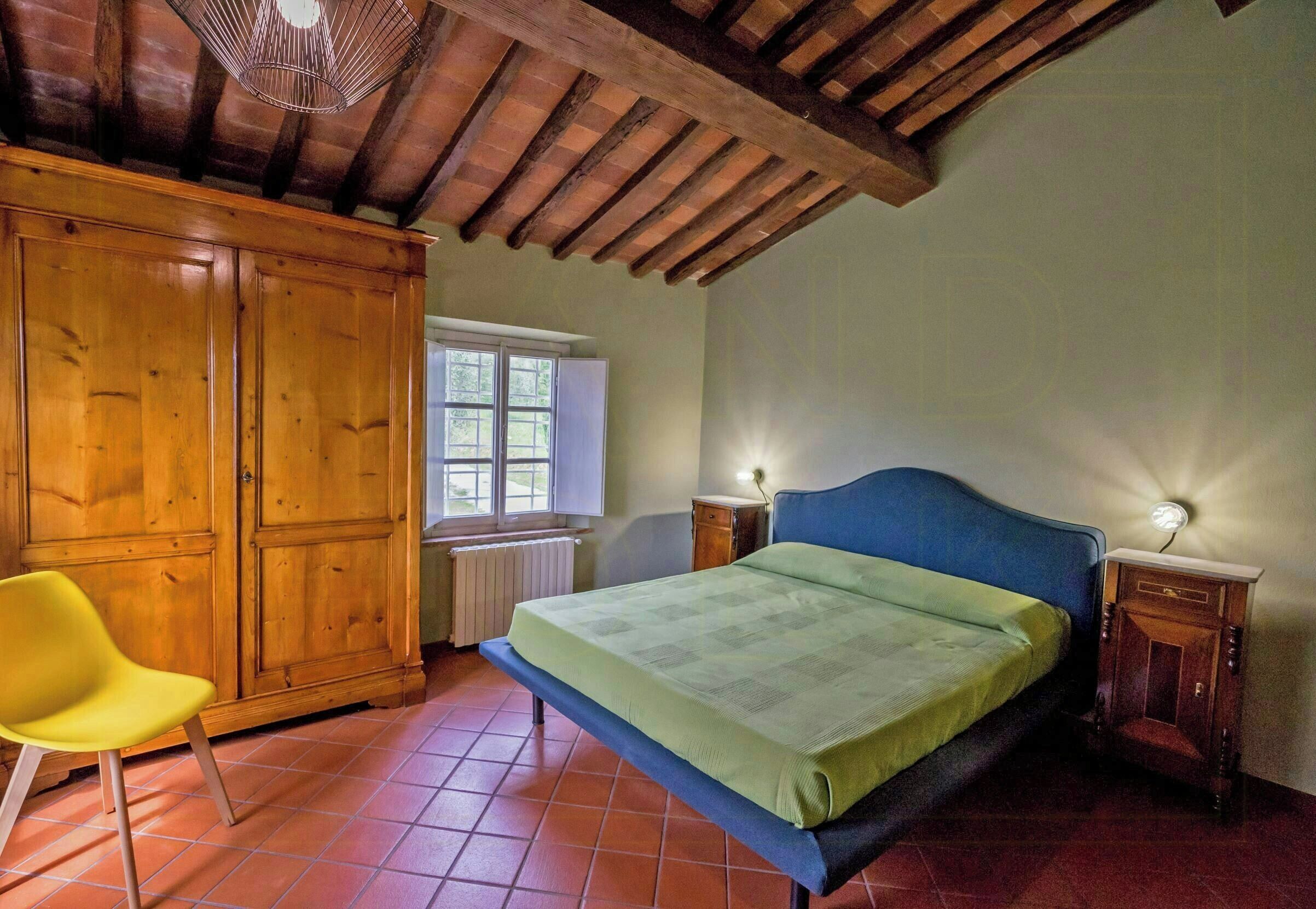 Een slaapkamer met een bed, een houten kledingkast, een stoel en een raam.
