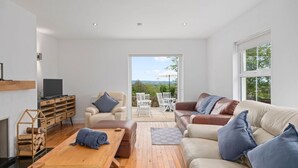 A modern living room with a fireplace, wooden furniture, a sofa with cushions, and a view of the outdoors through a glass door. - Hilltop View by Escape Ordinary (Lisbellaw, Enniskillen)