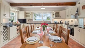 A spacious kitchen with white cabinets, a wooden dining table set for six, and a large window providing natural light. - Hilltop View by Escape Ordinary (Lisbellaw, Enniskillen)