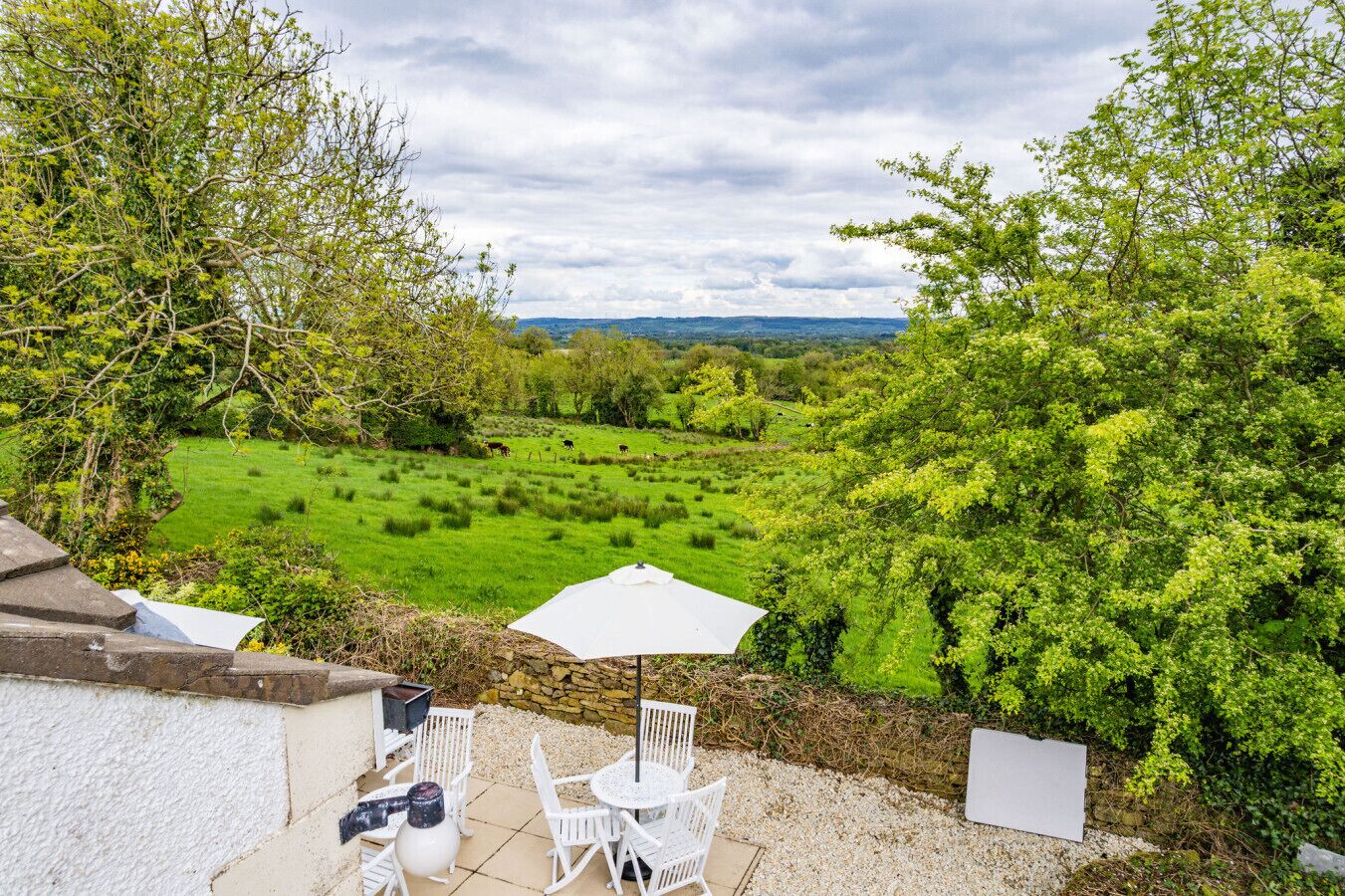 A patio with outdoor furniture and a white umbrella overlooking a green landscape.