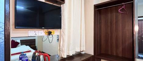 A hotel room with a TV, a wooden desk, a wardrobe, and a bed.