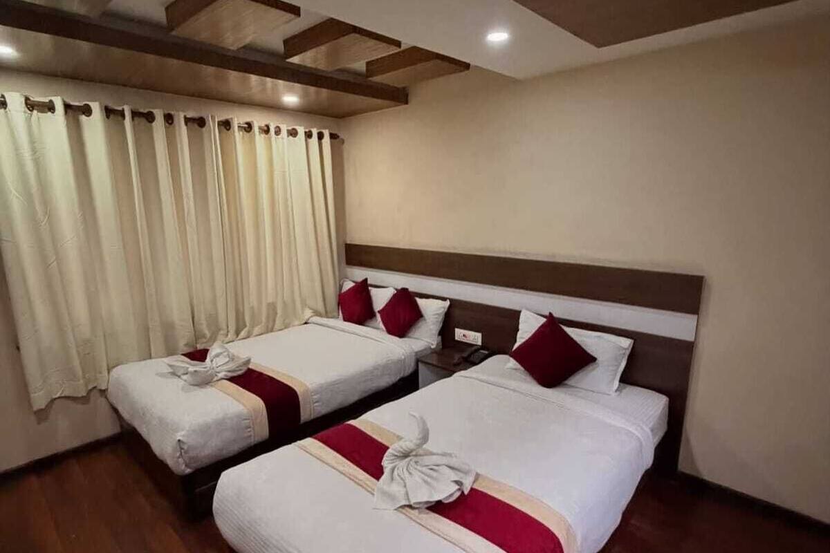 A hotel room with two beds, wooden flooring, a wooden ceiling with recessed lighting, and a window with curtains.