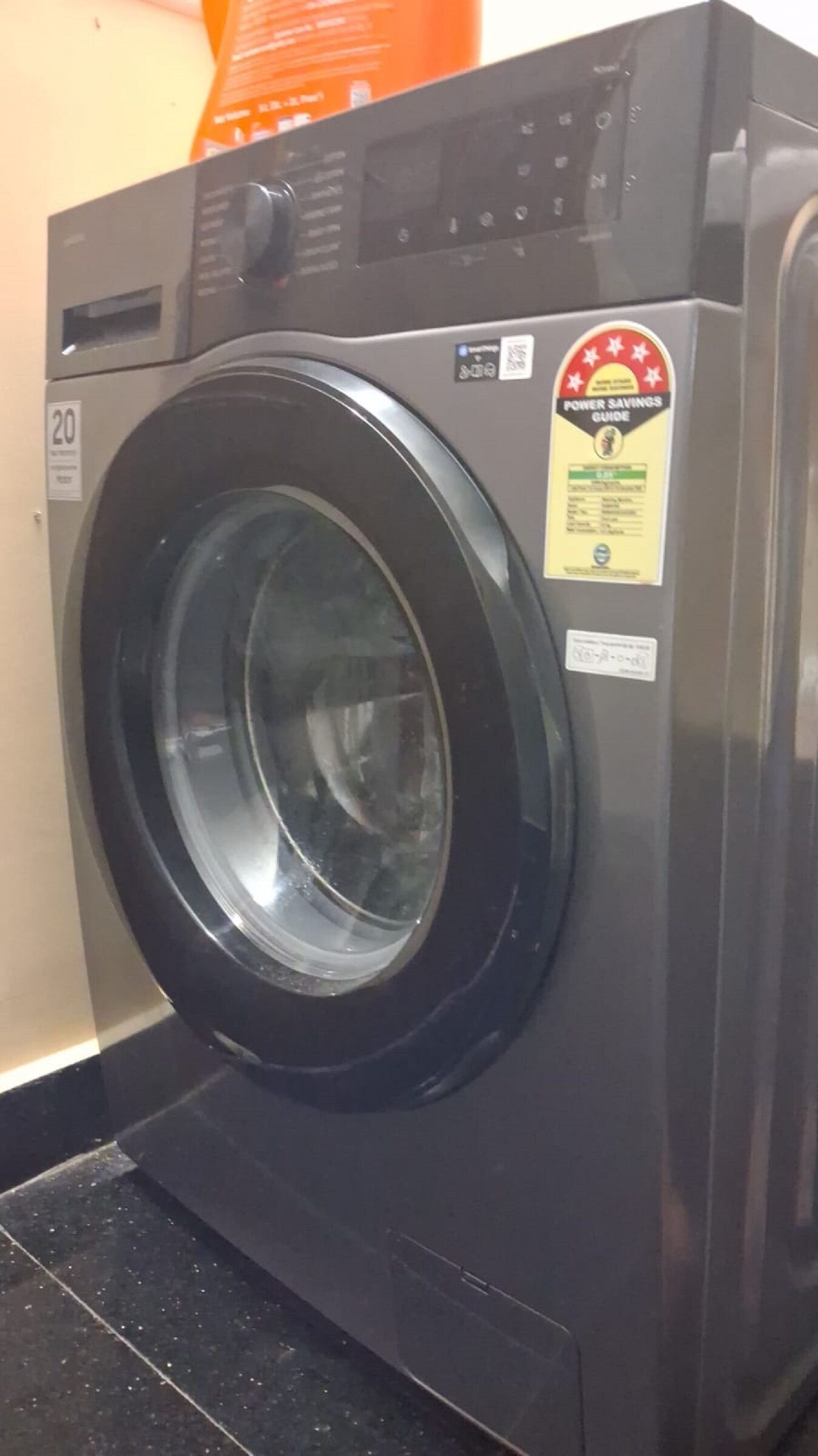 A front-loading washing machine with a front control panel, a power savings guide sticker, and a model number sticker.