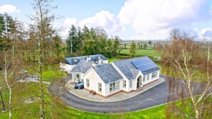 Ein Haus mit einer geschwungenen Auffahrt, Solaranlagen und einer kleinen Sitzgelegenheit im Freien.