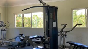 A gym with various exercise equipment, large windows, and a ceiling light fixture. - Apartamento playa, piscina vabaro (Punta Cana)