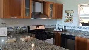 A kitchen with granite countertops, wooden cabinets, a stainless steel stove, and a dishwasher. - Apartamento playa, piscina vabaro (Punta Cana)