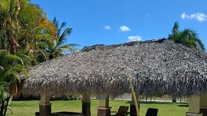 A thatched-roof structure with lounge chairs, a stone pathway, and palm trees. - Apartamento playa, piscina vabaro (Punta Cana)