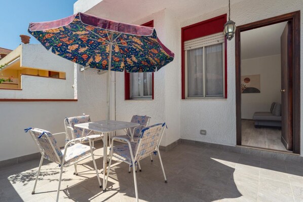 A patio with a table and chairs, an umbrella, and a door leading to an interior room.