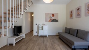 Un salon moderne avec un escalier, un téléviseur à écran plat, un canapé, un meuble et des œuvres d’art murales.
