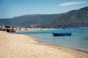 A beach with a boat, sandy shore, and mountains in the background. - A cozy apartment of approximately 90 square meters, spread over two levels connected by stairs, accommodating up to 6 people.The property is located in Torre Faro, a charming seaside village about 15 km from Messina, where the Ionian and Tyrrhenian Seas  (Messina)