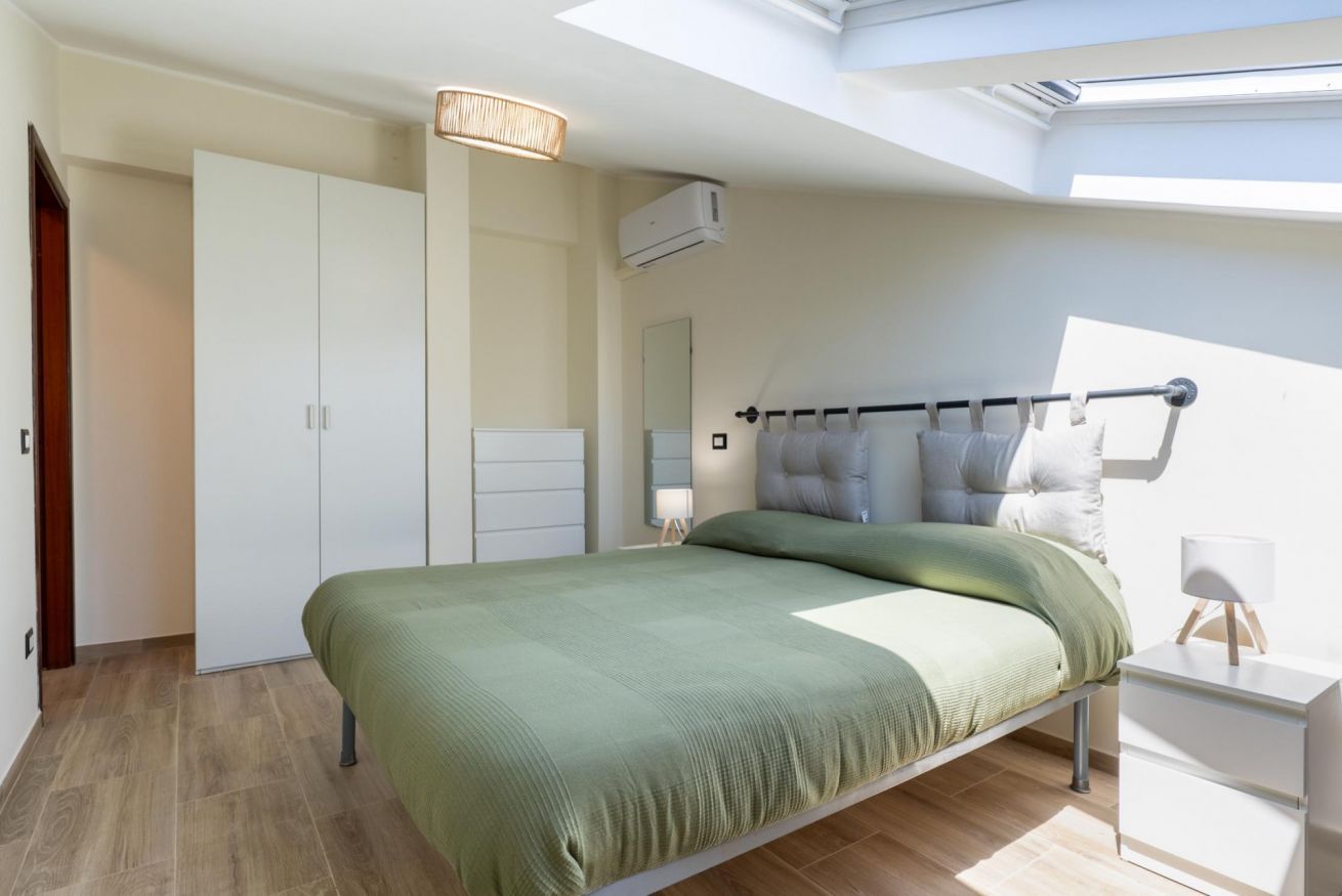 Ein Schlafzimmer mit Bett, Kleiderschrank, Nachttisch, Lampe und einem Oberlicht.