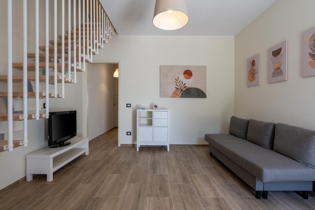 A modern living room with a staircase, a flat-screen TV, a sofa, a cabinet, and wall art.