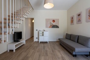 A modern living room with a staircase, a flat-screen TV, a sofa, a cabinet, and wall art.
