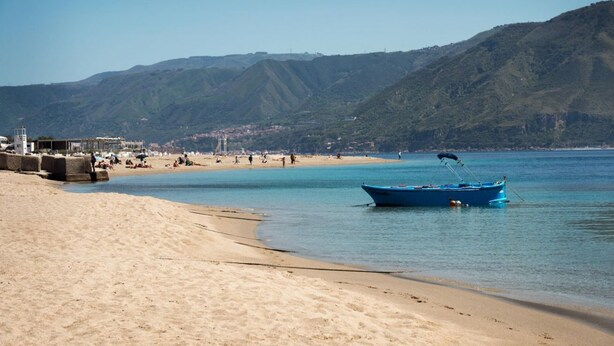 Une plage avec un bateau, un rivage sablonneux et des montagnes en arrière-plan.