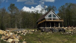 Une cabane dotée d’un balcon, entourée d’une forêt et de grands rochers.
