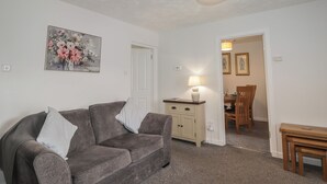 A living room with a sofa, a lamp, a painting, and a dining area with a table and chairs. - 3 Bruaich Cottages (Strathpeffer)