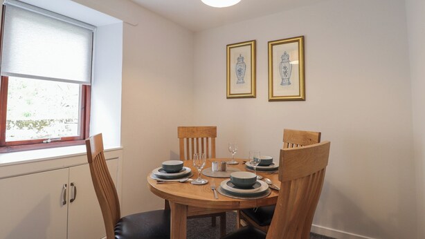 A dining area with a round wooden table, four chairs, and a window with blinds. - 3 Bruaich Cottages (Strathpeffer)