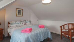 A bedroom with a sloped ceiling, a bed with floral bedding, a wooden chair, and a framed picture on the wall. - 3 Bruaich Cottages (Strathpeffer)