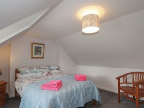 Un dormitorio con techo inclinado, una cama con ropa de cama floral, una silla de madera y un cuadro en la pared.