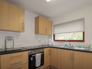 Una cocina moderna con armarios de madera, encimera negra, horno empotrado y ventana con persianas.