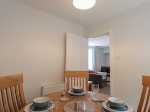 Un comedor con una mesa dispuesta para cuatro, una silla, un radiador y una puerta que da a otra habitación.