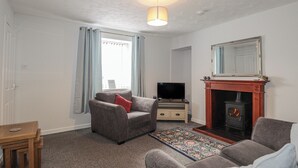A living room with a sofa, a television, a fireplace, and a window with curtains. - 3 Bruaich Cottages (Strathpeffer)