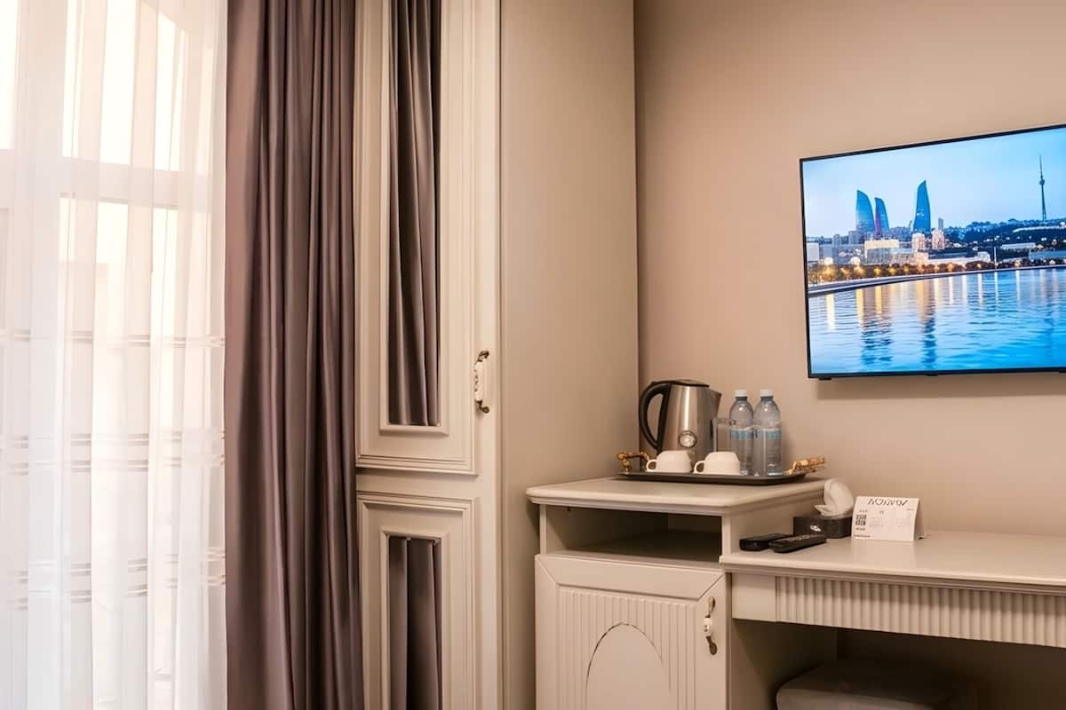 A hotel room with a bed, a desk with a flat-screen TV, a window with curtains, and a cityscape view.