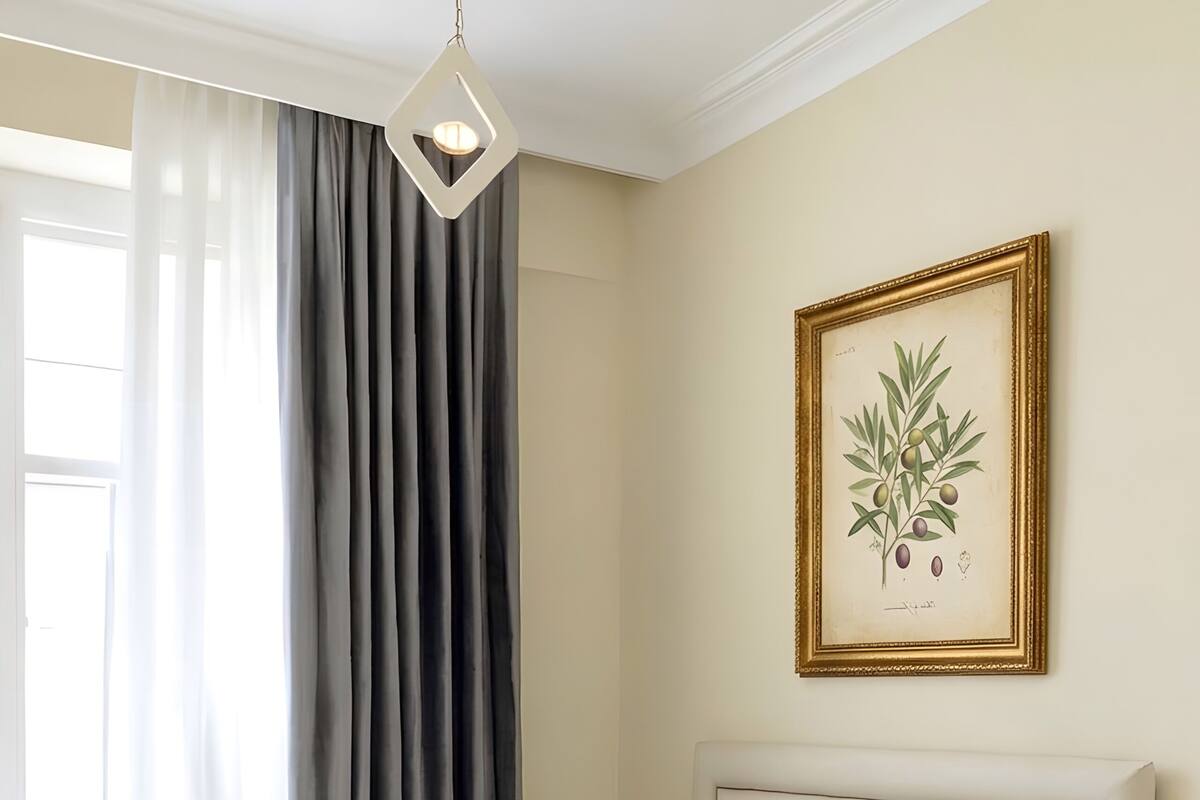 A neatly made bed with a grey throw, a bedside table with a plant, and a framed botanical illustration on the wall.