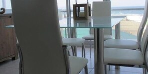 Ein Essbereich mit Glastisch und Stühlen, Blick auf den Ozean und einem Holzschrank.