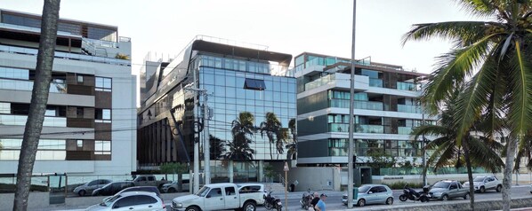 A modern building with a glass facade, a red bike lane, and parked vehicles. - Flat beira-mar Cabo Branco com rooftop AH211 (João Pessoa)