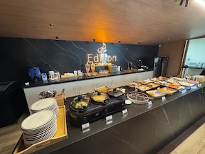 Un comptoir de buffet avec un pare-feu en marbre, un néon indiquant « Edition Coffee Shop », ainsi que divers aliments et ustensiles.