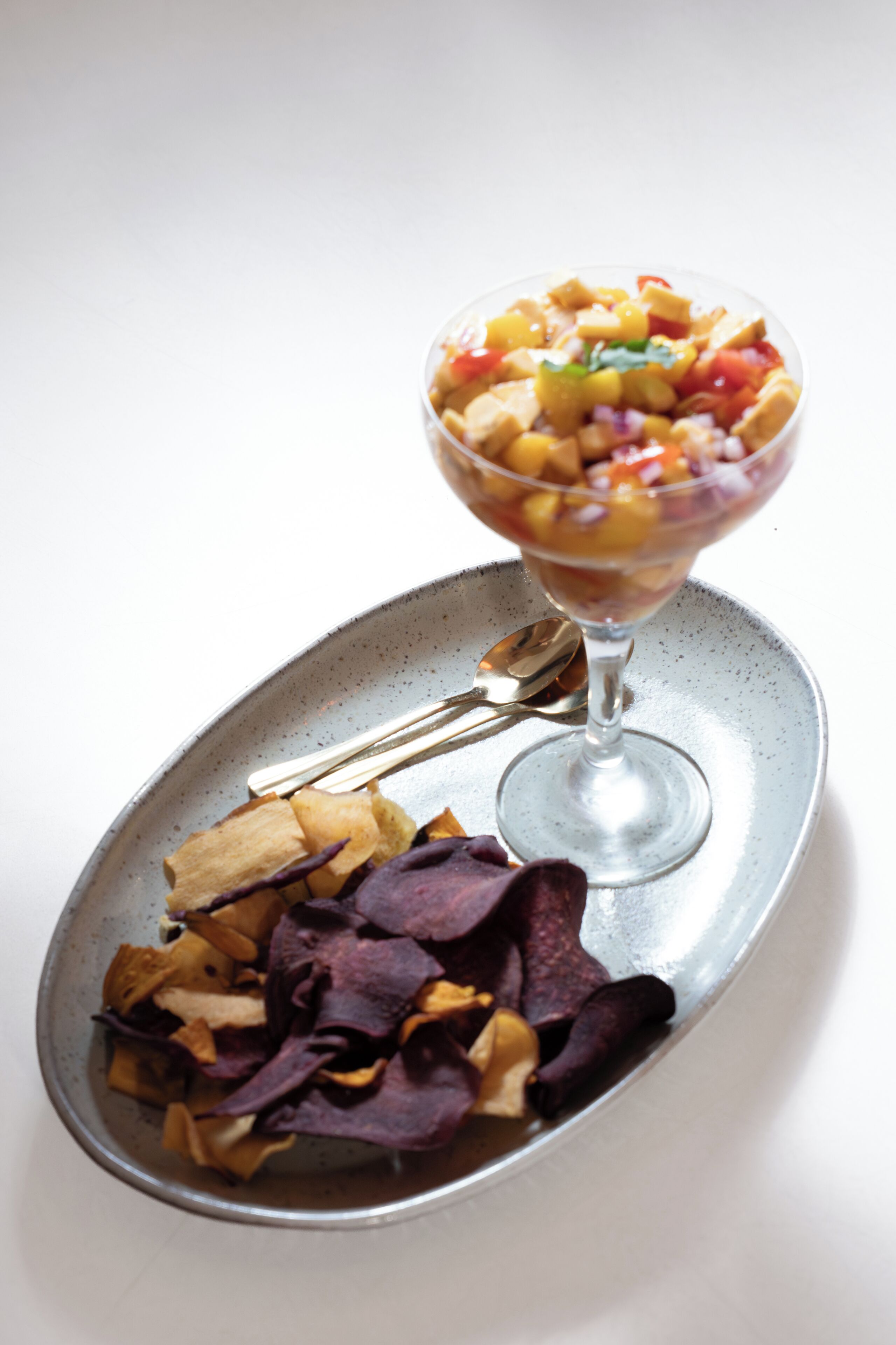 A dessert in a glass bowl on a plate with a spoon, accompanied by dried fruit pieces.