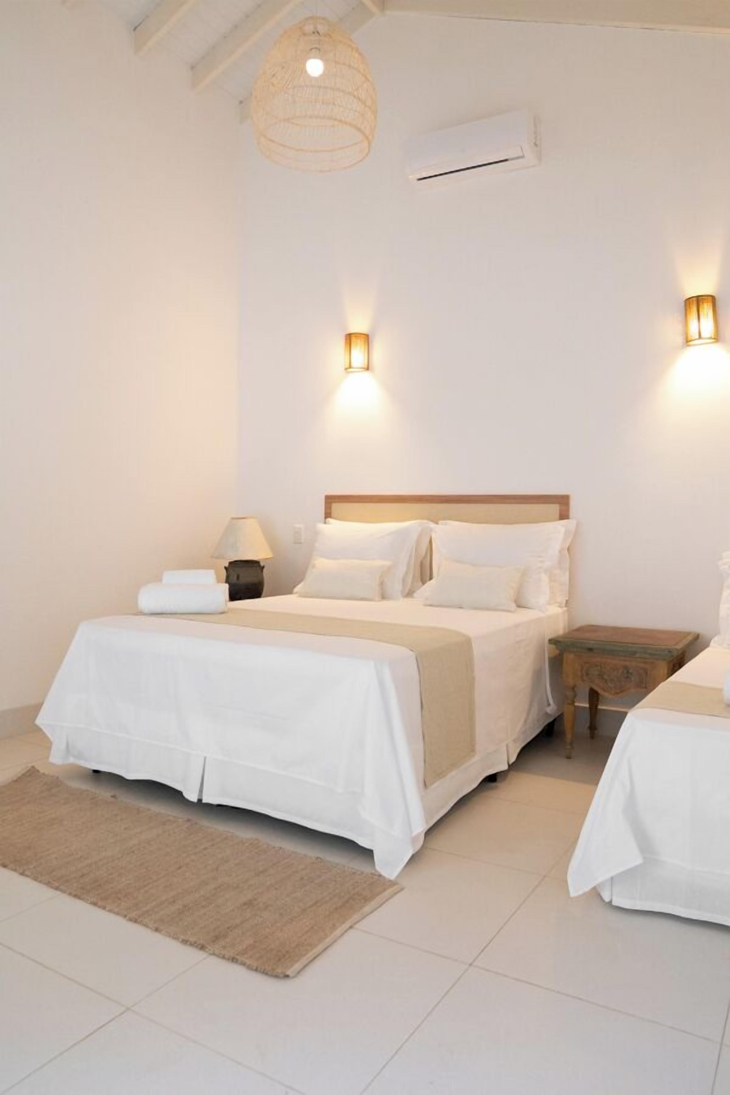 Quarto com cama, mesas de cabeceira, abajur e luminária pendente.