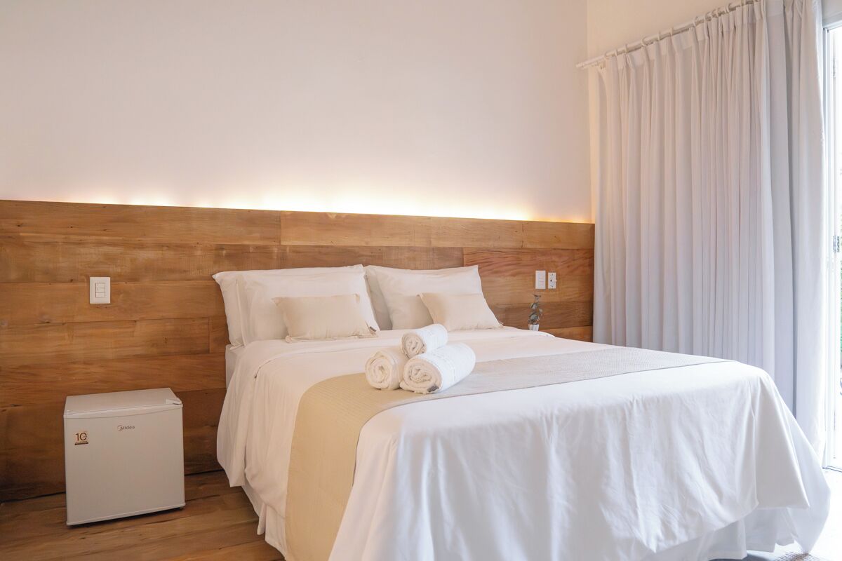 Ein Hotelzimmer mit einem hölzernen Kopfteil, einem Bett mit weißer Bettwäsche, einem Nachttisch und einem kleinen weißen Gerät.