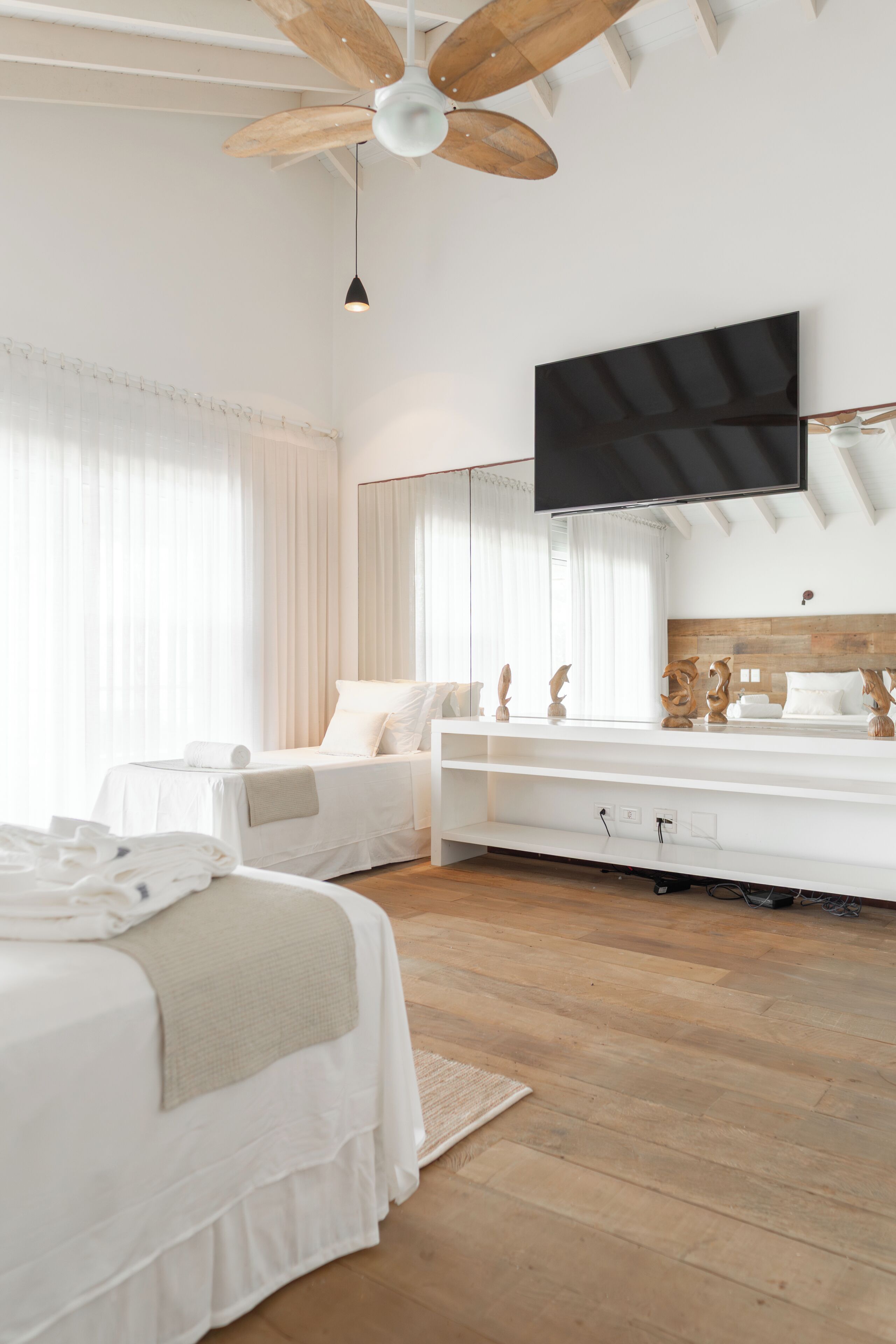 Ein modernes Hotelzimmer mit Deckenventilator aus Holz, einem großen Flachbildfernseher an der Wand, einem Bett mit weißer Bettwäsche und Holzboden.