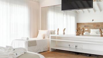 Ein modernes Hotelzimmer mit Deckenventilator aus Holz, einem großen Flachbildfernseher an der Wand, einem Bett mit weißer Bettwäsche und Holzboden.