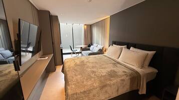 A hotel room with a large bed, a TV, a seating area with a table and chairs, and a view through a glass door.