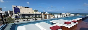 Une piscine à débordement située sur le toit, avec des chaises longues et une vue sur le paysage urbain.