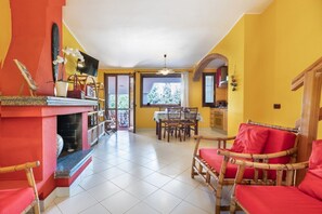 Ein Wohnzimmer mit Kamin, einem Essbereich und einer durchgehenden Tür erkennbaren Küche.