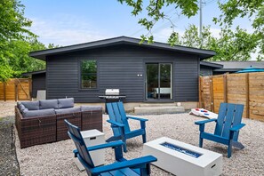 Una casa moderna con fachada oscura, un patio con mobiliario exterior y una parrilla.