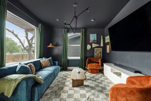 Una sala de estar con un sofá azul, un sillón naranja, una mesa de centro de madera y un televisor de pantalla plana.